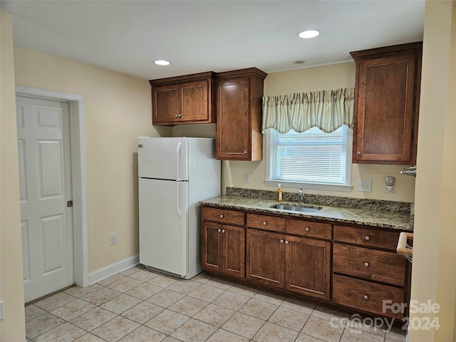 kitchen featuring dark stone counters, white refrigerator, light tile patterned flooring, sink, and dark brown cabinetry