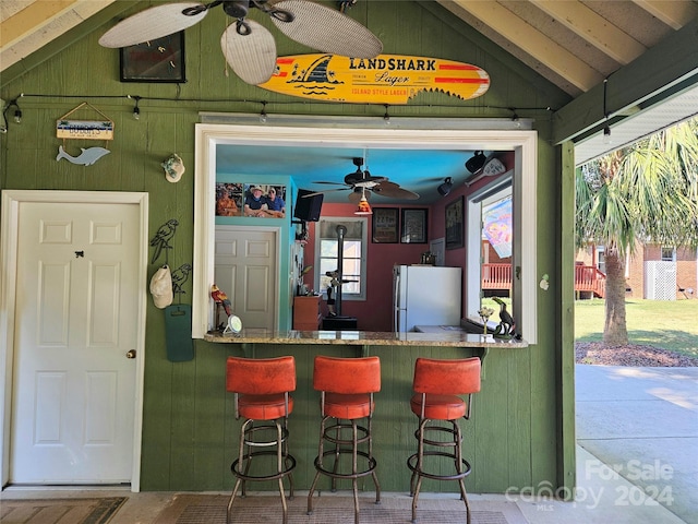 bar featuring vaulted ceiling, white refrigerator, wood walls, and ceiling fan