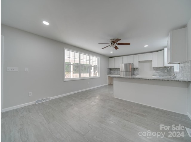 kitchen with stainless steel fridge, sink, light stone counters, kitchen peninsula, and white cabinetry