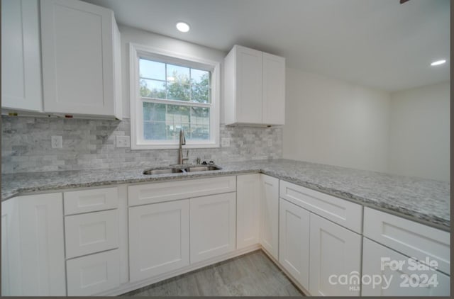 kitchen featuring light stone counters, sink, kitchen peninsula, white cabinetry, and backsplash