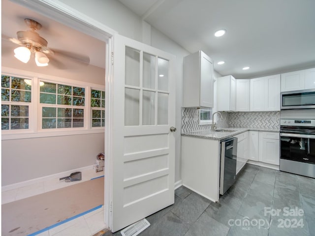 kitchen with light stone countertops, decorative backsplash, stainless steel appliances, white cabinets, and sink