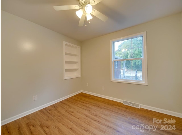 unfurnished room featuring ceiling fan, built in shelves, and light hardwood / wood-style floors