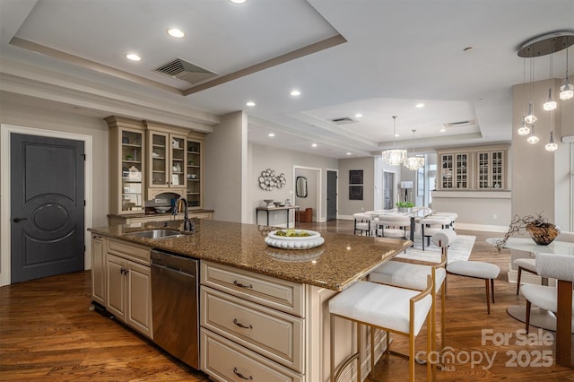 kitchen featuring decorative light fixtures, sink, a kitchen island with sink, stainless steel dishwasher, and a tray ceiling