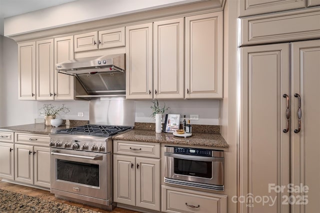 kitchen featuring stainless steel appliances, cream cabinets, dark stone countertops, and dark hardwood / wood-style flooring