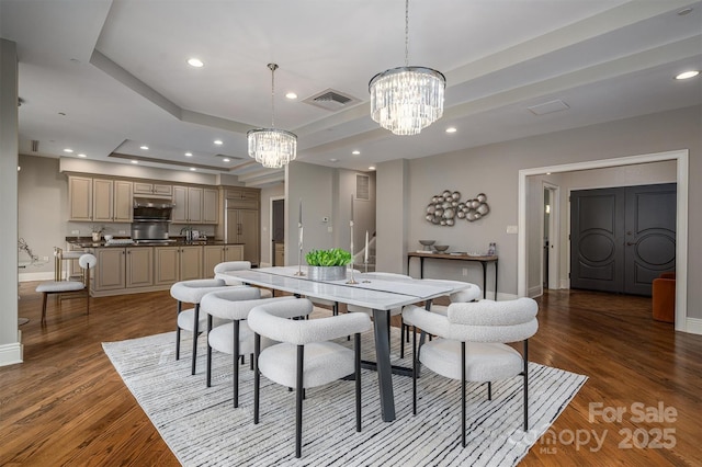 dining area with a raised ceiling, dark hardwood / wood-style floors, and an inviting chandelier