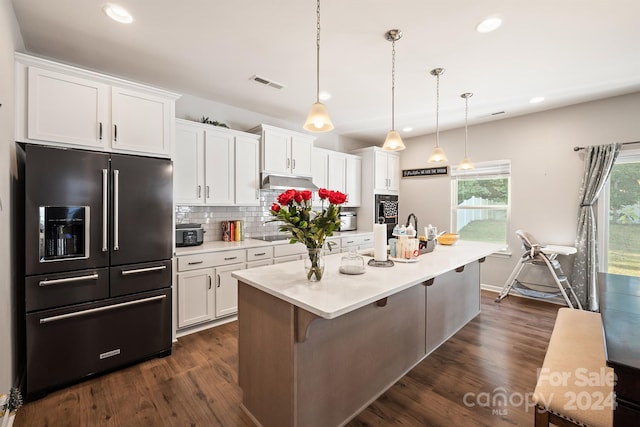 kitchen with high end fridge, an island with sink, white cabinetry, hanging light fixtures, and dark hardwood / wood-style flooring