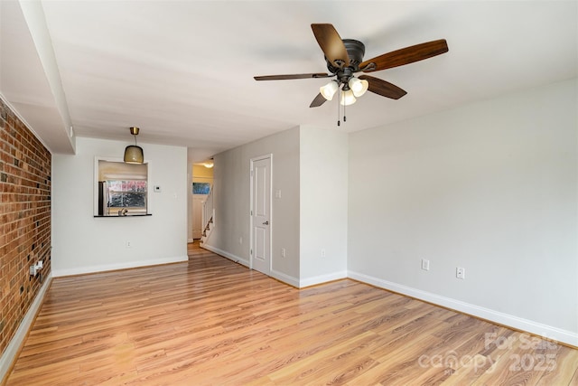 unfurnished room featuring ceiling fan, brick wall, and light hardwood / wood-style floors