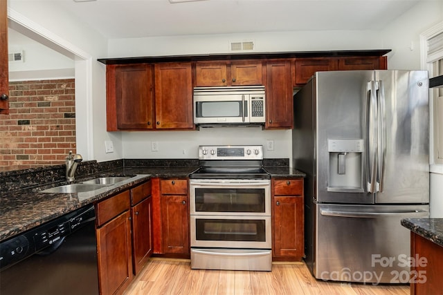 kitchen featuring dark stone countertops, sink, light hardwood / wood-style floors, and appliances with stainless steel finishes