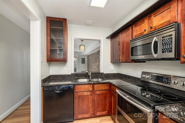 kitchen with appliances with stainless steel finishes, sink, dark stone countertops, and light hardwood / wood-style flooring