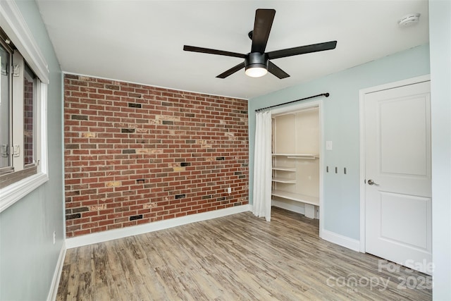 unfurnished bedroom featuring light hardwood / wood-style floors, a closet, ceiling fan, and brick wall