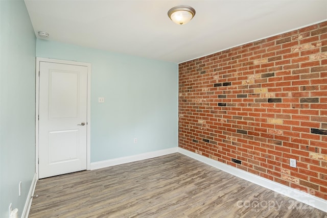 empty room with brick wall and hardwood / wood-style floors