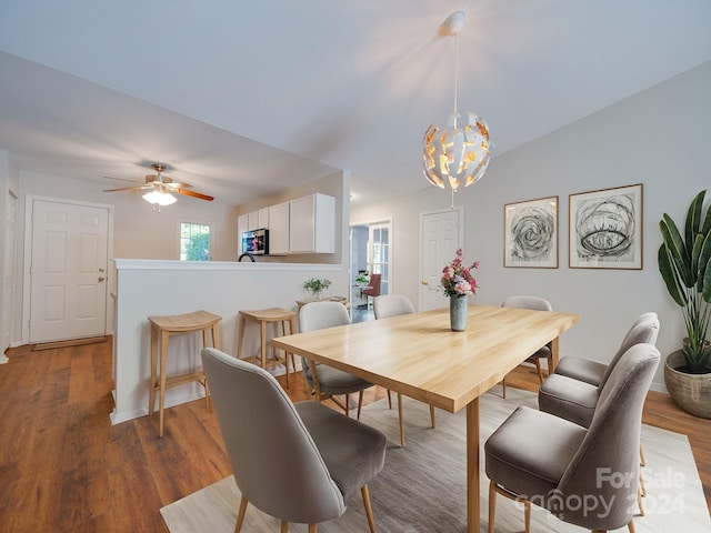 dining room with vaulted ceiling, ceiling fan with notable chandelier, and dark hardwood / wood-style flooring