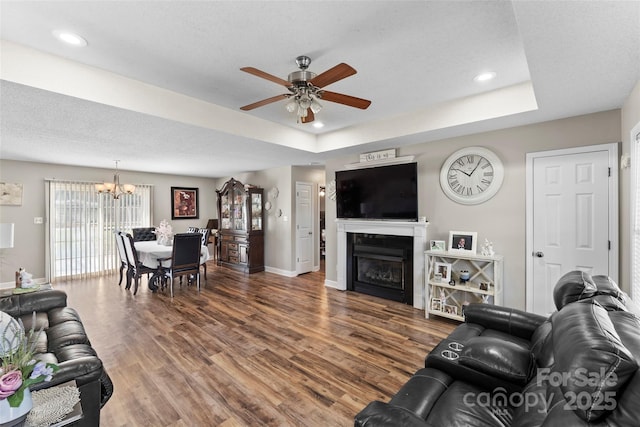 living room with a raised ceiling, hardwood / wood-style floors, a textured ceiling, and ceiling fan with notable chandelier