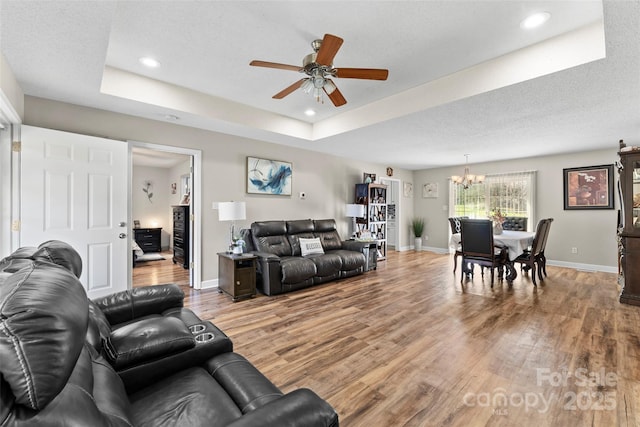 living room with hardwood / wood-style flooring, ceiling fan with notable chandelier, and a raised ceiling