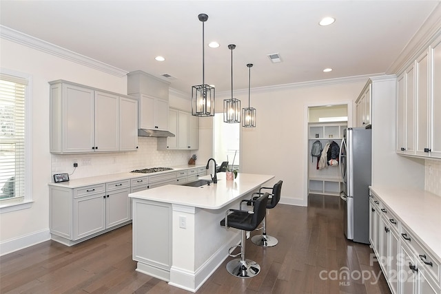 kitchen featuring a kitchen island with sink, dark wood-type flooring, stainless steel appliances, sink, and pendant lighting