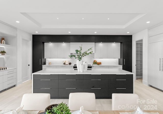 kitchen with white cabinets, light wood-type flooring, and a tray ceiling