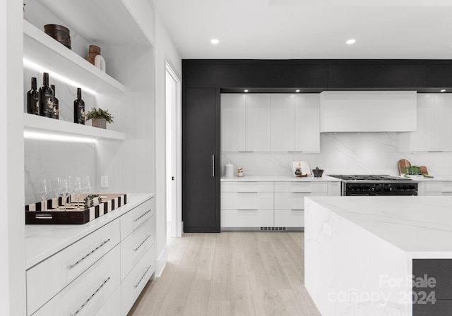 kitchen with stainless steel gas cooktop, tasteful backsplash, light hardwood / wood-style flooring, light stone countertops, and white cabinets