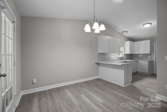 kitchen featuring backsplash, kitchen peninsula, pendant lighting, vaulted ceiling, and white cabinets