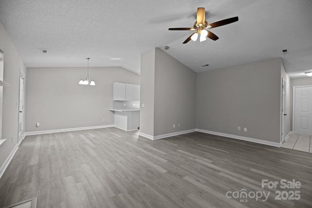 unfurnished living room with a textured ceiling, ceiling fan with notable chandelier, vaulted ceiling, and hardwood / wood-style flooring