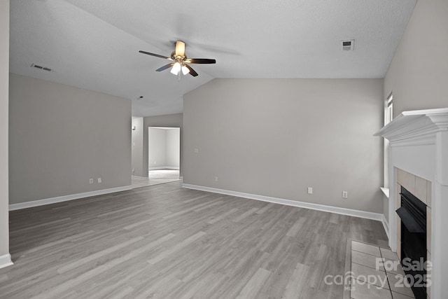 unfurnished living room with a tile fireplace, ceiling fan, a textured ceiling, vaulted ceiling, and light wood-type flooring