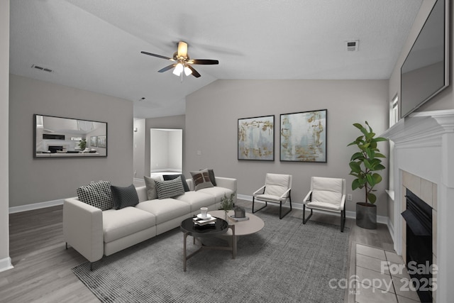 living room with a textured ceiling, ceiling fan, hardwood / wood-style flooring, lofted ceiling, and a tiled fireplace