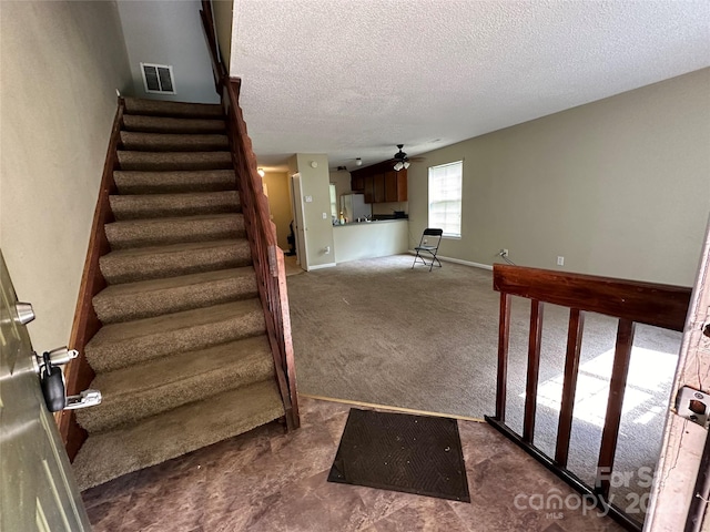 staircase with carpet, ceiling fan, and a textured ceiling