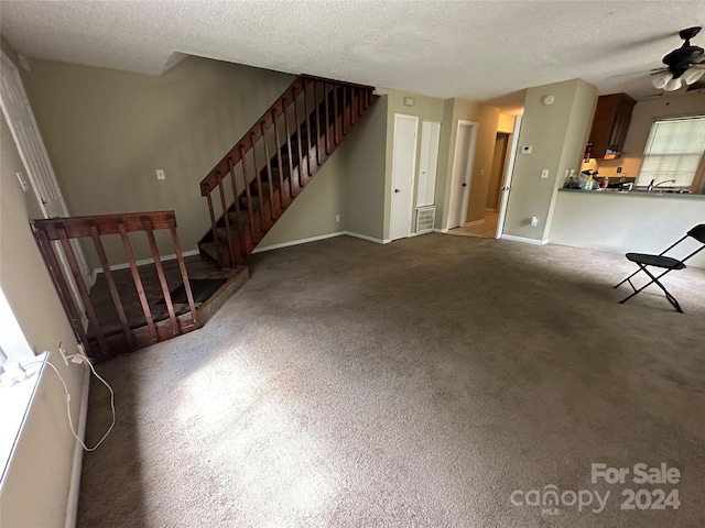 unfurnished living room featuring ceiling fan, a textured ceiling, and carpet flooring