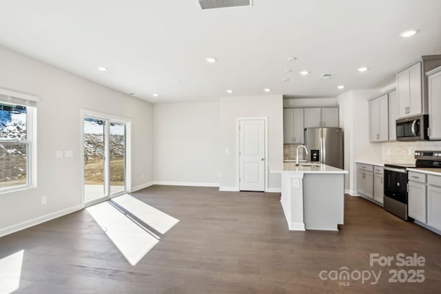 kitchen featuring dark wood-type flooring, appliances with stainless steel finishes, gray cabinets, and a kitchen island with sink