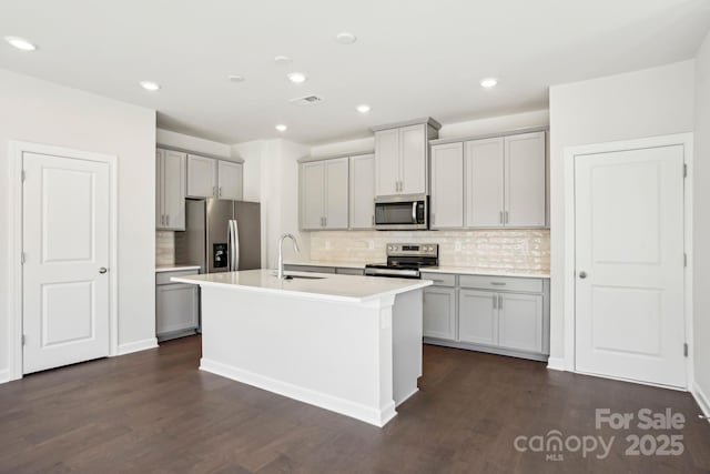 kitchen featuring appliances with stainless steel finishes, dark wood-type flooring, sink, a kitchen island with sink, and gray cabinetry