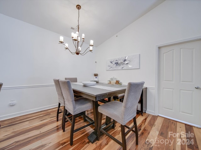 dining space with light hardwood / wood-style flooring, a chandelier, and vaulted ceiling