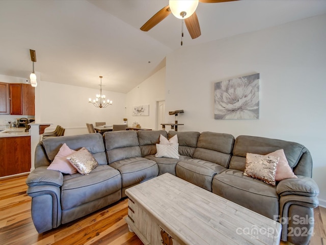 living room featuring ceiling fan with notable chandelier, light hardwood / wood-style floors, vaulted ceiling, and sink