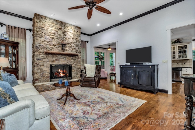 living room with hardwood / wood-style flooring, crown molding, ceiling fan, and a stone fireplace