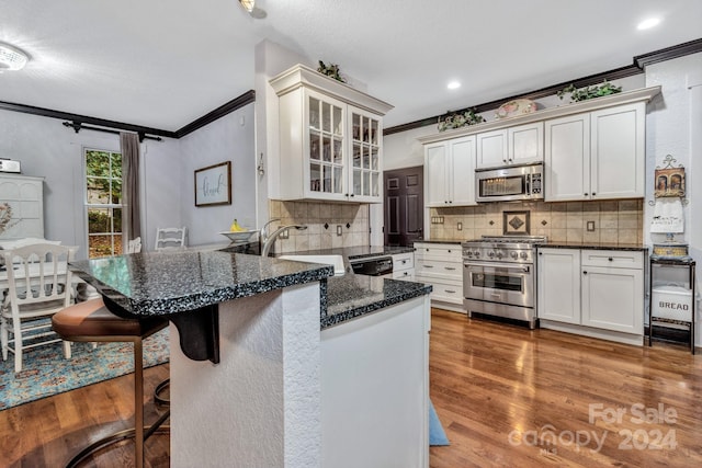 kitchen featuring appliances with stainless steel finishes, crown molding, a kitchen breakfast bar, and white cabinets