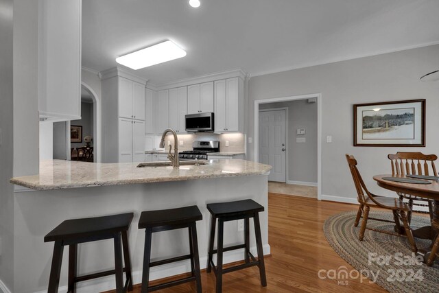 kitchen with light wood-type flooring, sink, ornamental molding, white cabinets, and appliances with stainless steel finishes