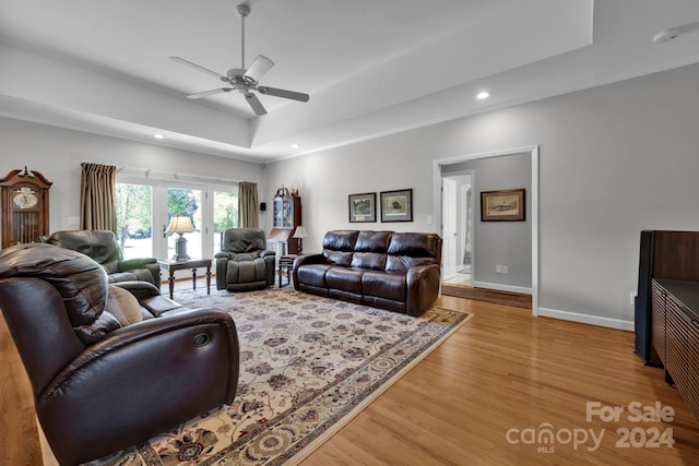 living room featuring light wood-type flooring, ceiling fan, and a raised ceiling