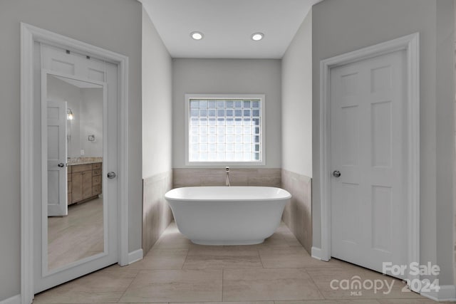 bathroom featuring vanity, a bathtub, tile patterned flooring, and tile walls