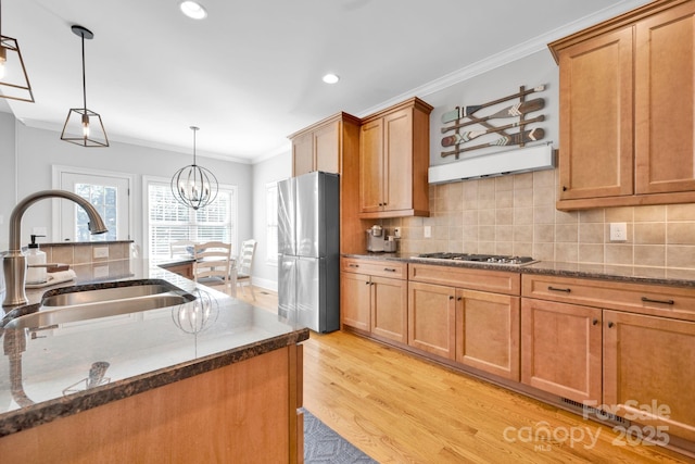 kitchen with appliances with stainless steel finishes, pendant lighting, tasteful backsplash, sink, and light wood-type flooring