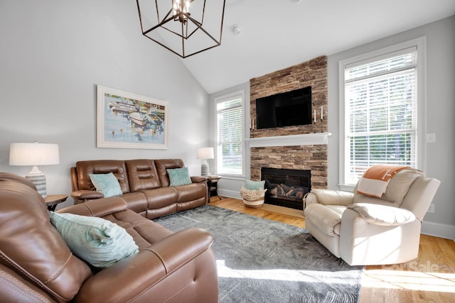 living room featuring lofted ceiling, wood-type flooring, a stone fireplace, and a chandelier