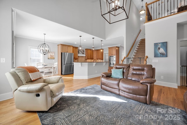 living room with an inviting chandelier, a towering ceiling, ornamental molding, and light wood-type flooring