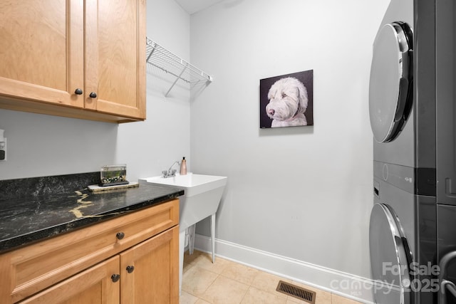 laundry area featuring cabinets, stacked washer and clothes dryer, and light tile patterned floors