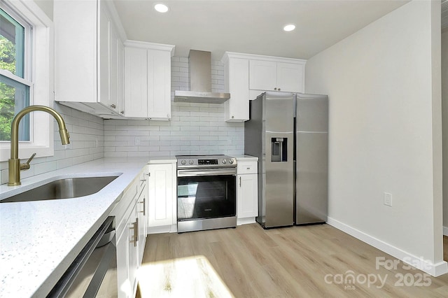 kitchen featuring sink, appliances with stainless steel finishes, white cabinetry, light stone counters, and wall chimney exhaust hood