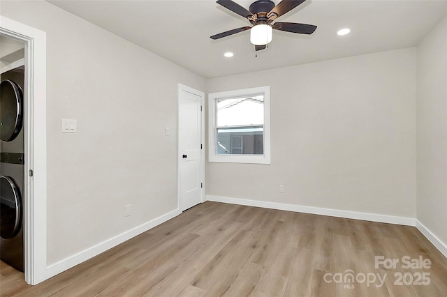 empty room with stacked washer and clothes dryer, ceiling fan, and light wood-type flooring