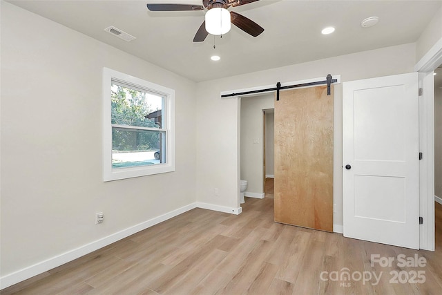 unfurnished bedroom featuring a barn door, ceiling fan, and light hardwood / wood-style flooring