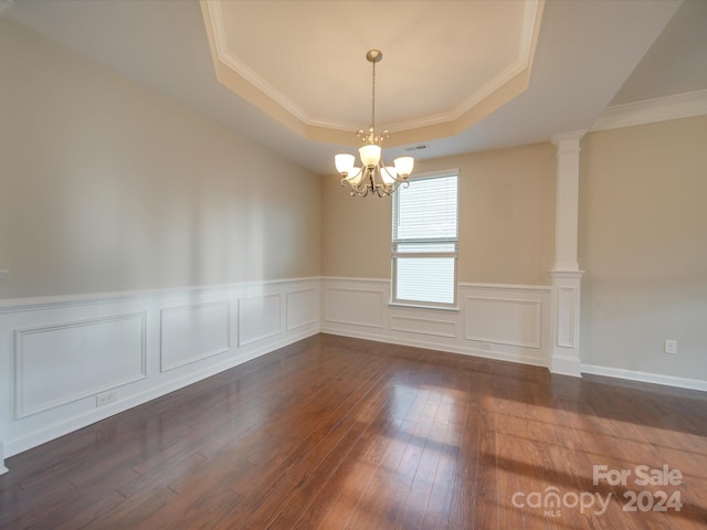 unfurnished room featuring ornamental molding, decorative columns, an inviting chandelier, a raised ceiling, and dark hardwood / wood-style flooring