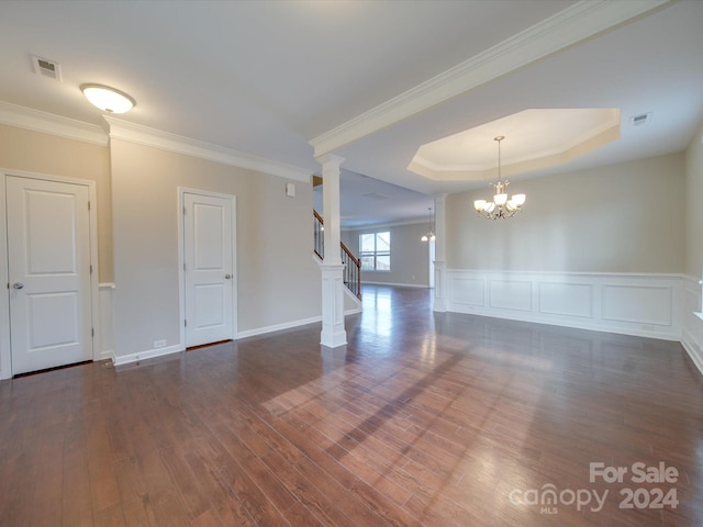 unfurnished room with an inviting chandelier, a tray ceiling, dark hardwood / wood-style floors, ornate columns, and crown molding