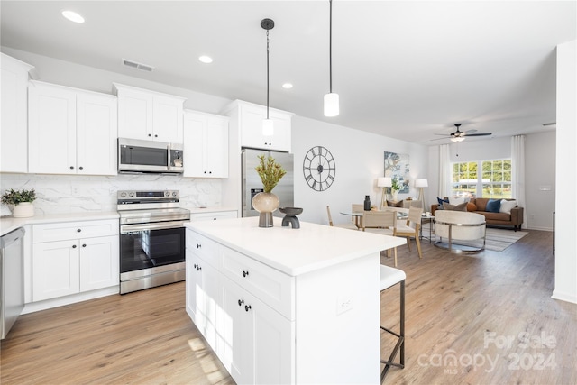 kitchen with appliances with stainless steel finishes, a kitchen island, light hardwood / wood-style flooring, white cabinetry, and hanging light fixtures