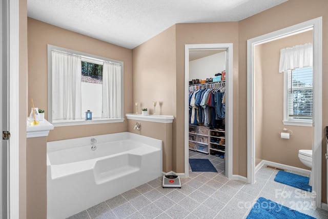 bathroom with a textured ceiling, a bathing tub, toilet, and a wealth of natural light