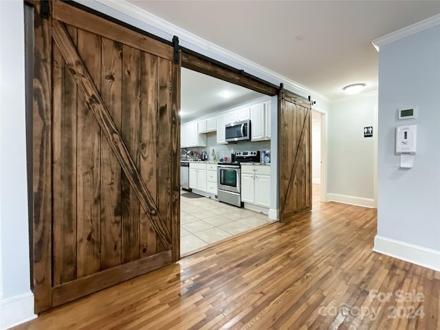 kitchen with light hardwood / wood-style floors, white cabinetry, appliances with stainless steel finishes, crown molding, and a barn door