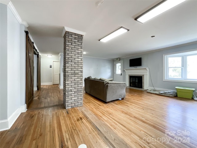 unfurnished living room featuring a barn door, crown molding, a large fireplace, decorative columns, and hardwood / wood-style floors