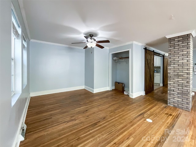 interior space featuring a barn door, wood-type flooring, crown molding, and ceiling fan